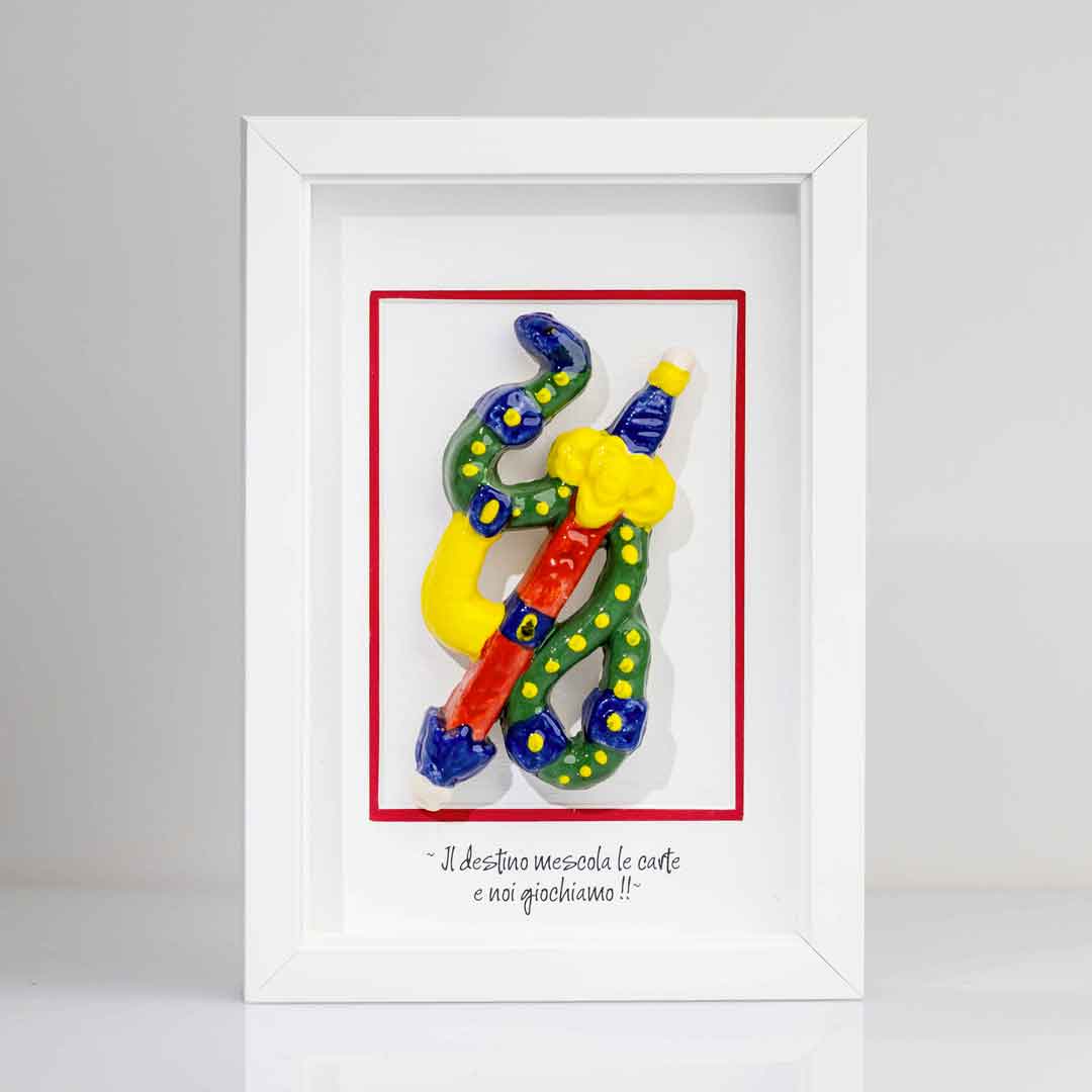 Quadro con cornice bianca contenente una riproduzione tridimensionale in ceramica dell'Asso di Spade delle carte napoletane. Raffigura una spada con impugnatura gialla e azzurra, avvolta da un elemento sinuoso verde a pois gialli. In basso è presente la scritta in corsivo: "Il destino mescola le carte e noi giochiamo!!". 